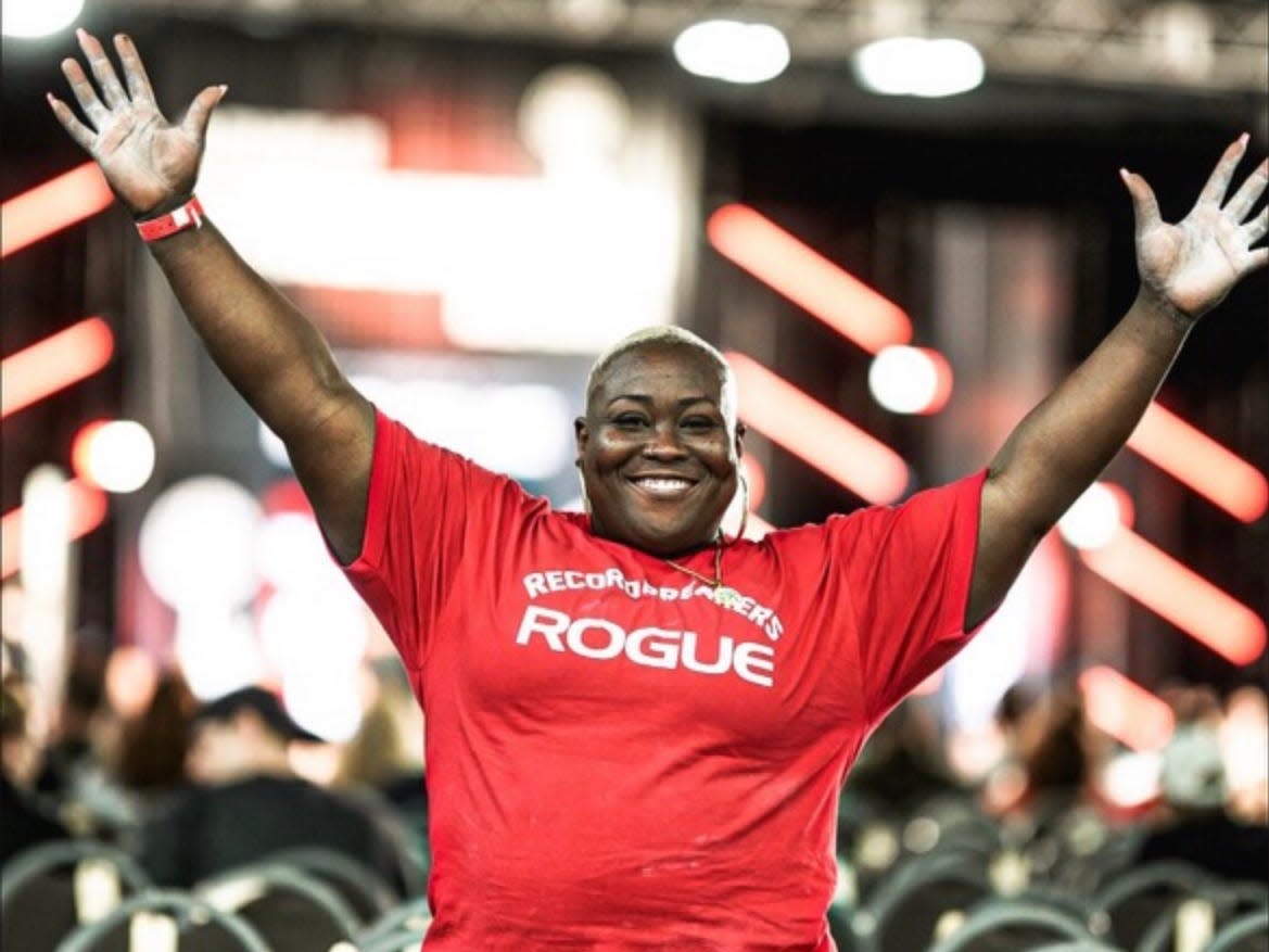 world record powerlifter Tamara Walcott standing in red leggings and a red "Rogue" T-shirt, covered in chalk, with arms raised