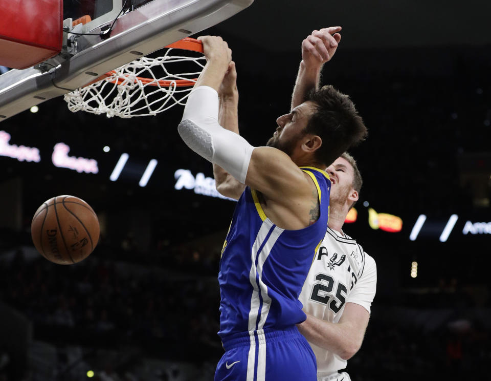 Golden State Warriors center Andrew Bogut (12) is hit across the face as he score against San Antonio Spurs center Jakob Poeltl (25) during the first half of an NBA basketball game, in San Antonio, Monday, March 18, 2019. (AP Photo/Eric Gay)