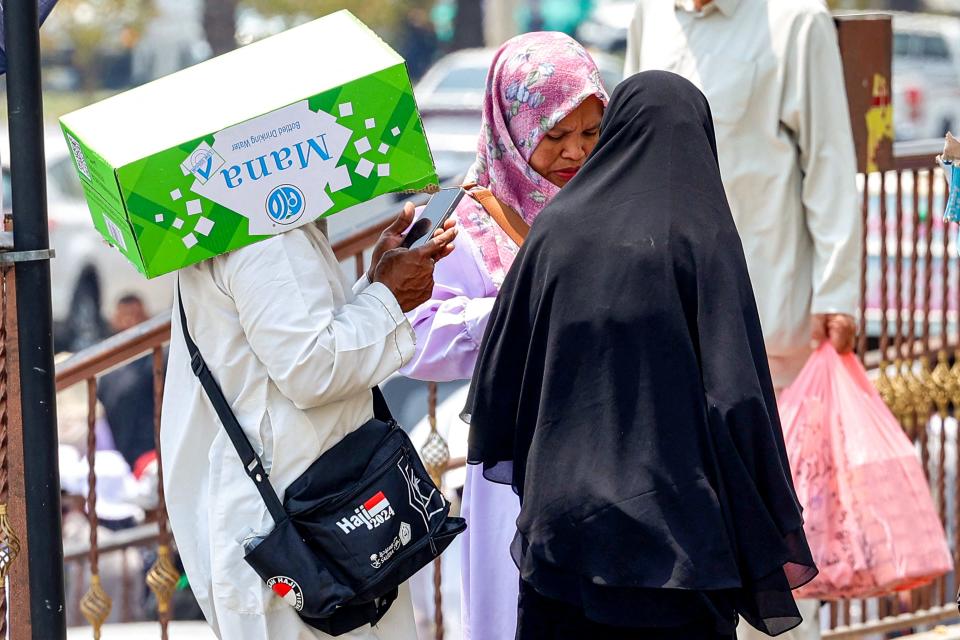 A man shades his head with a cardboard box while surfing on his phone next to other women in Saudi Arabia's holy city of Mecca on June 20, 2024.