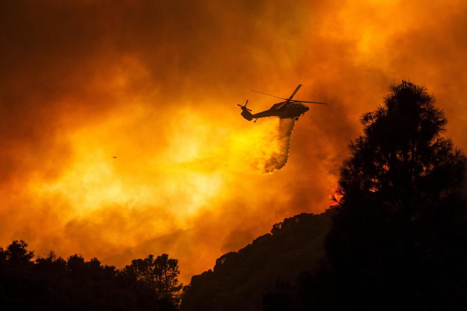 FILE - In this Aug. 12, 2020, file photo, a helicopter drops water on the Lake Hughes Fire in Angeles National Forest north of Santa Clarita, Calif. A huge forest fire that prompted evacuations north of Los Angeles flared up around noon Saturday, Aug. 15, sending up a cloud of smoke as it headed toward thick, dry brush in the Angeles National Forest. Evacuation orders remain in effect for the western Antelope Valley because erratic winds in the forecast could push the fire toward homes. Record-breaking heat is possible through the weekend, with triple-digit temperatures and unhealthy air predicted for many parts of the state. (AP Photo/Ringo H.W. Chiu, File)