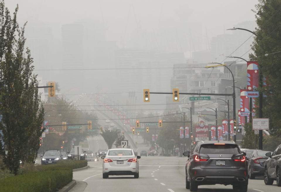 Heavy smog envelops a major thoroughfare in Vancouver as traffic lights pierce the darkness.