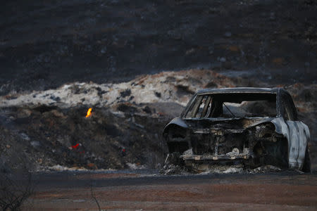 The burnt wreckage of a vehicle is seen along a road as a flames are seen, in the aftermath of the Woolsey fire in Malibu, Southern California, U.S. November 11, 2018. REUTERS/Mario Anzuoni