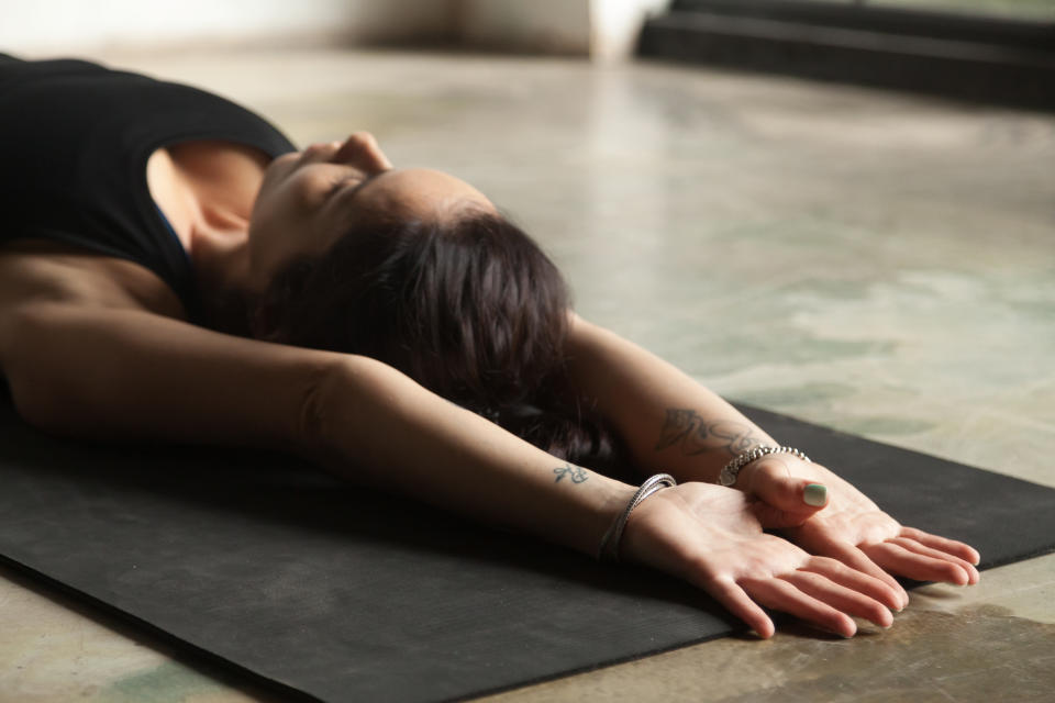 Young woman practicing yoga, stretching on mat, palms facing upward, relaxing after stressful situation in a restorative exercise, body and mind resting pose, indoor close up image, floor background