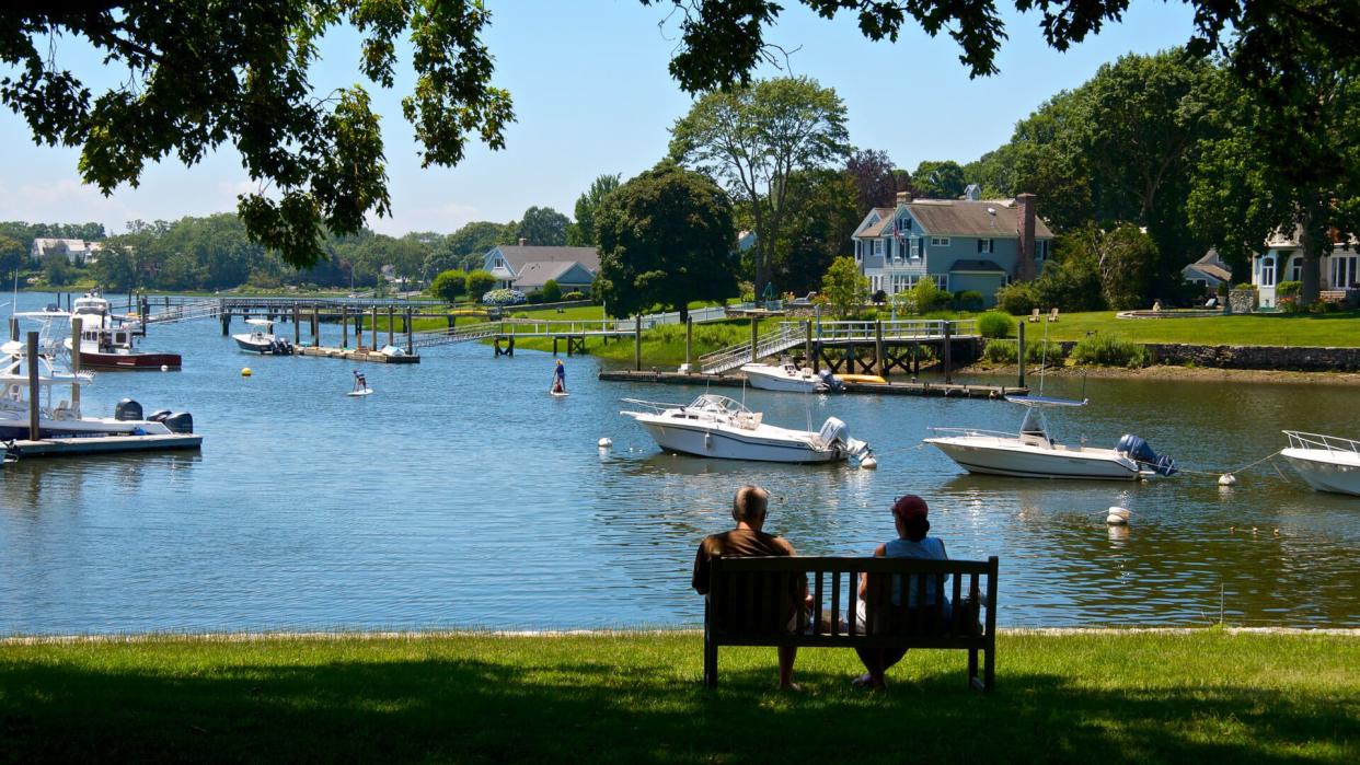 Connecticut, USA - July 05, 2013: A couple sit on a bench in  cool shade at the shoreline of a Long Island Sound inlet  in summer time, Rowayton, Connecticut, New England.