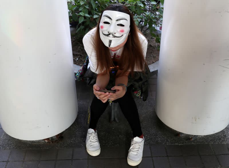 FILE PHOTO: An anti-government protester wearing a Guy Fawkes mask checks her phone during the "Lest We Forget" rally in Hong Kong