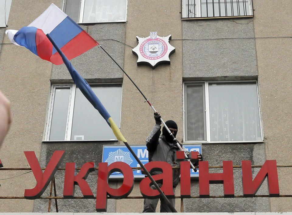 A pro-Russian man places a Russian flag over a police station during its mass storming in the eastern Ukrainian town of Horlivka on Monday, April 14, 2014. The text reads: Ukrainian police station in Horlivka". Several government buildings has fallen to mobs of Moscow loyalists in recent days as unrest spreads across the east of the country. (AP Photo/Efrem Lukatsky)