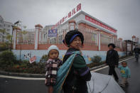 Ethnic minority women walk with their child near a kindergarten with a banner which reads "I'm a China doll, can speak Mandarin" at the apartment houses compound built by the Chinese government in Yuexi county, southwest China's Sichuan province on Sept. 11, 2020. China's ruling Communist Party says its initiatives have helped to lift millions of people out of poverty. But they can require drastic changes, sometimes uprooting whole communities. They fuel complaints the party is trying to erase cultures as it prods minorities to embrace the language and lifestyle of the Han who make up more than 90% of China’s population. The words on top read "Preschool speak Mandarin, Not afraid of talking and reading." (AP Photo/Andy Wong)