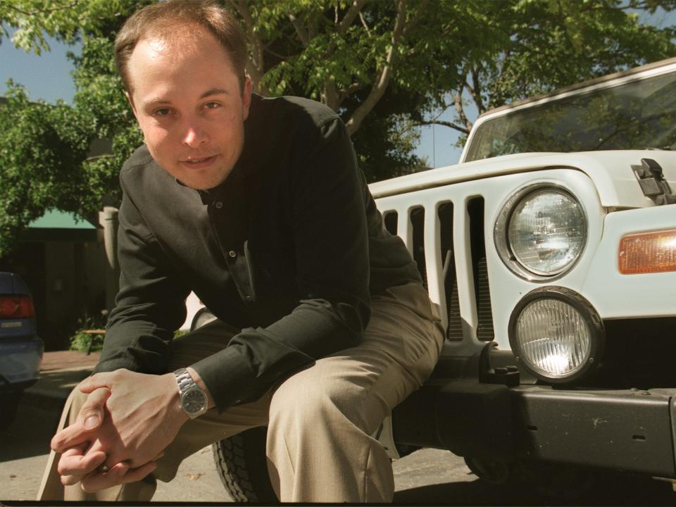 Elon Musk sitting on a car bumper.