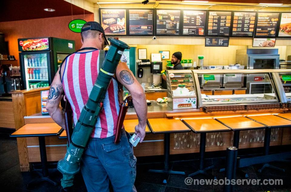 Steve Wagner of Smithfield carries an inert AT-4 anti-tank weapon and two pistols while paying for sandwiches at a Subway in downtown Raleigh Saturday morning, May 9, 2020. A group of about 11 mostly-armed demonstrators protesting the stay-at-home order marched around downtown Raleigh and ordered sandwiches.