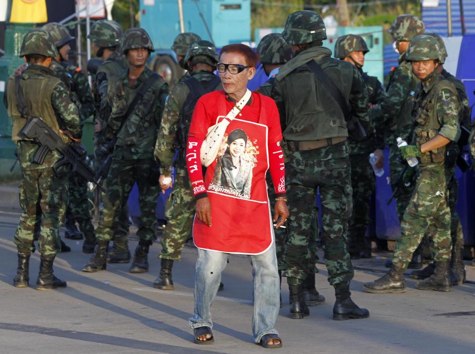 A member of the pro-government "red shirt" group walks past Thai soldiers at an encampment in Nakhon Pathom province on the outskirts of Bangkok May 22, 2014. Thailand's army chief General Prayuth Chan-ocha took control of the government in the coup on Thursday saying the army had to restore order and push through reforms, two days after he declared martial law. REUTERS/Chaiwat Subprasom (THAILAND - Tags: POLITICS CIVIL UNREST MILITARY)