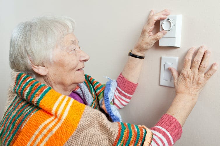 Elderly woman wrapped in blanket adjusting thermostat