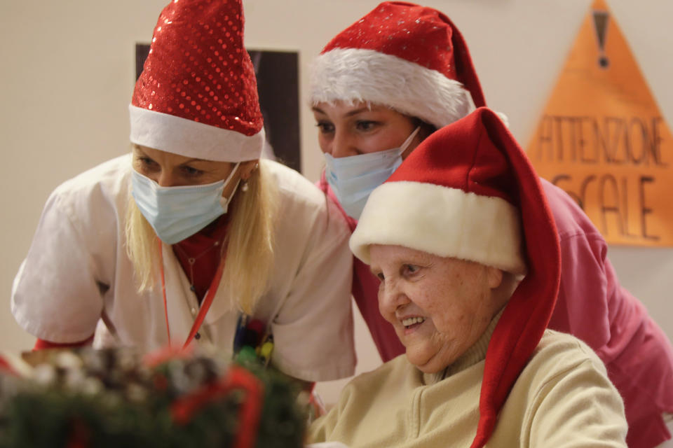 Elsa Giovanelli, 89, is flanked by carer Michela Valle, center, and director Maria Giulia Madaschi as she talks on a video call with Jessica Marino, a donor unrelated to her, who bought and sent her a Christmas present through an organization dubbed "Santa's Grandchildren", at the Martino Zanchi nursing home in Alzano Lombardo, one of the area that most suffered the first wave of COVID-19, in northern Italy, Saturday, Dec. 19, 2020. (AP Photo/Luca Bruno)