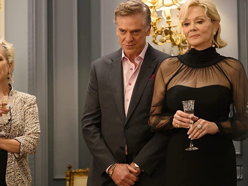 Actress Jean Smart appears as her character Deborah Vance in a black dress in "Hacks," standing next to a man and woman at what appears to be a party.