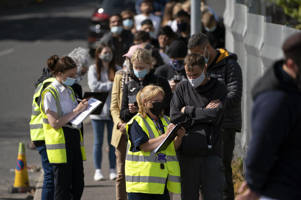 FILE - In this May 18, 2021, file photo, people queue for vaccinations against coronavirus at the ESSA academy in Bolton, England. Coronavirus infections, hospitalizations and deaths are plummeting across much of Europe. Vaccination rates are accelerating, and with them, the promise of summer vacations. (AP Photo/Jon Super, File)