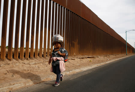 A migrant woman, part of a caravan of thousands traveling from Central America en route to the United States, carries her belongings on her head as she walks past the border fence between Mexico and United States while moving to a new shelter in Mexicali, Mexico November 19, 2018. REUTERS/Kim Kyung-Hoon