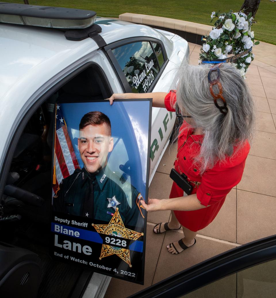 Polk County sheriff's communications editor Robin Jenkins places a poster of Polk County Deputy Blane Lane in a memorial patrol car before a press conference Tuesday.