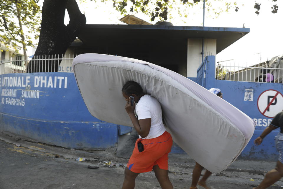 A woman, carrying a mattress, walks past a charred police station that was set on fire by armed gangs, in Port-au-Prince, Haiti, Thursday, March 7, 2024. (AP Photo/Odelyn Joseph)