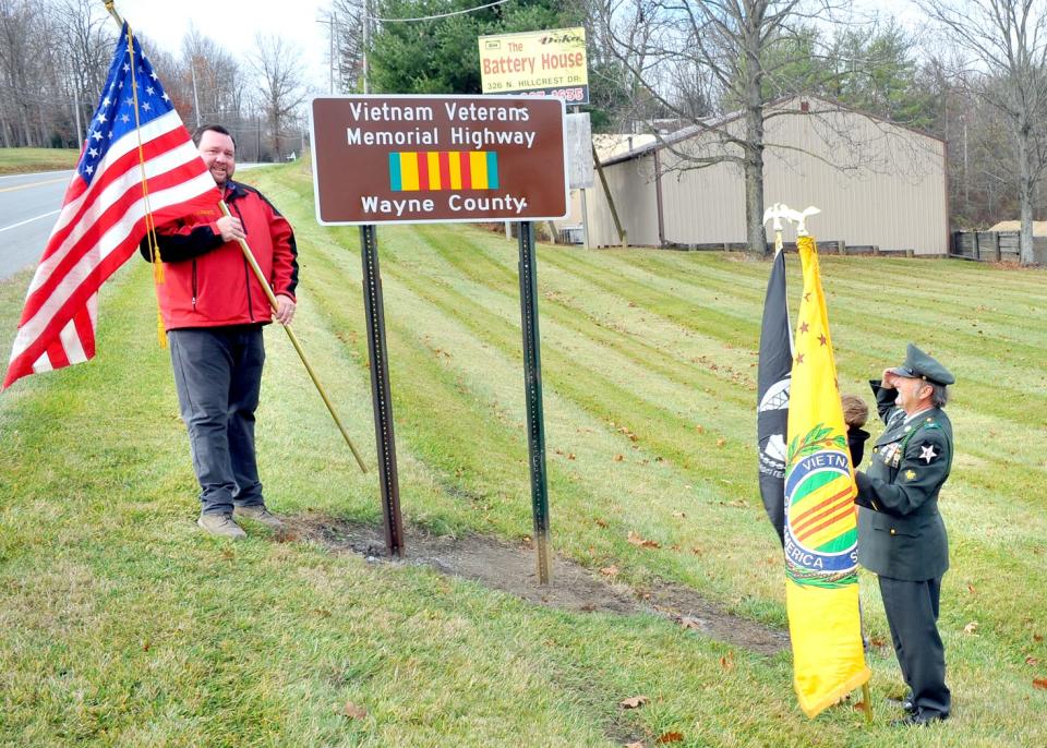 Matt Martin (left) holds the American flag next to the newly dedicated Wayne County Vietnam Veterans Memorial Highway as Vietnam-era veteran Jeff Sampsel salutes. Sampsel worked for two years to get the memorial finalized.
