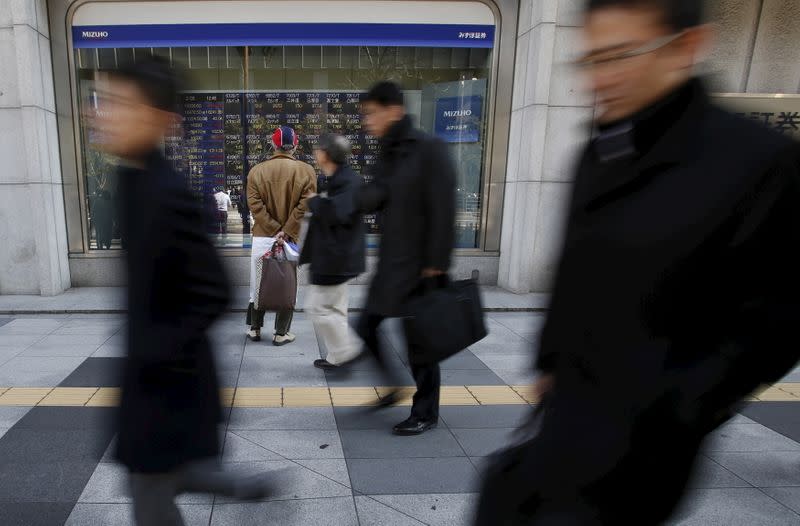 A pedestrian looks at various stock prices outside a brokerage in Tokyo