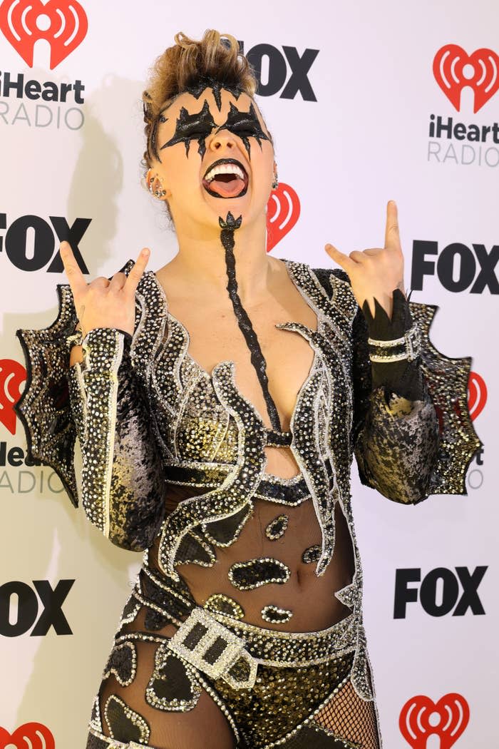 Person in a sequined outfit with unique patterns, posing with a peace sign and tongue out