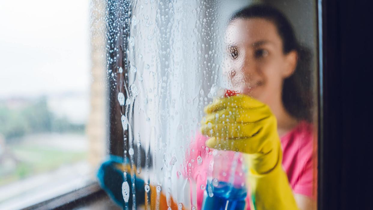 Young woman wiping windows at home.