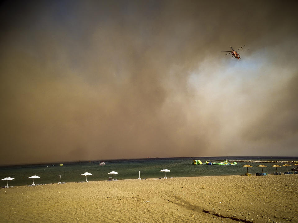 A firefighting helicopter flies over a beach during a forest fire on the island of Rhodes, Greece, Saturday, July 22, 2023. A large wildfire burning on the Greek island of Rhodes for a fifth day has forced authorities to order an evacuation of four locations, including two seaside resorts. (Argyris Mantikos/Eurokinissi via AP)