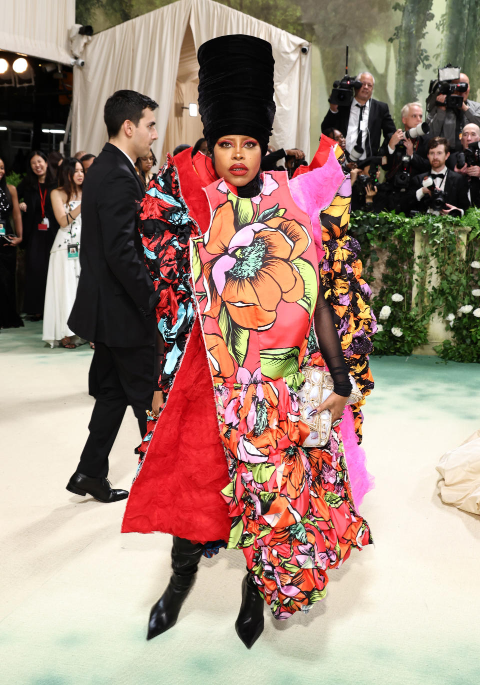 Erykah Badu at a celebrity event, wearing an elaborate outfit with floral patterns and vibrant designs, paired with a tall black headpiece