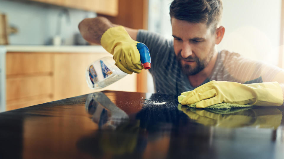 Shot of a young man cleaning the kitchen counter at home.