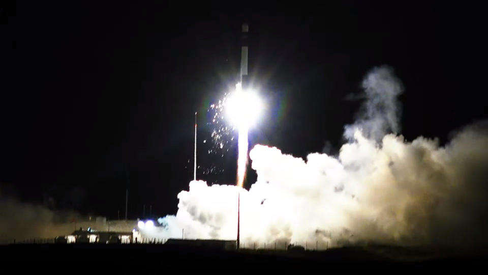 A white and black  Rocket Lab Electron rocket launches into the nighttime sky with sparks spitting out from it on Feb. 18, 2024.