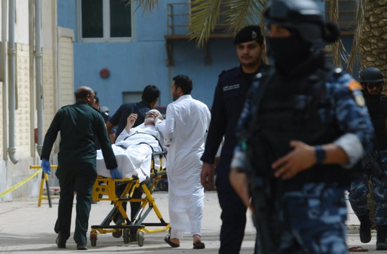 Kuwaiti emergency personnel pull a man on stretchers past security forces outside the Shiite Al-Imam al-Sadeq mosque after it was targeted by a suicide bombing during Friday prayers on June 26, 2015, in Kuwait City