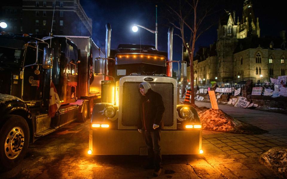 TOPSHOT - A truck driver listens to the engine of his truck during a protest over pandemic health rules and the Trudeau government, outside the parliament of Canada in Ottawa on February 14, 2022. - Canadian Prime Minister Justin Trudeau on Monday invoked rarely used emergency powers to bring an end to trucker-led protests against Covid health rules, after police arrested 11 people with a "cache of firearms" blocking a border crossing with the United States. (Photo by Ed JONES / AFP) (Photo by ED JONES/AFP via Getty Images) - Ed Jones/Getty Images