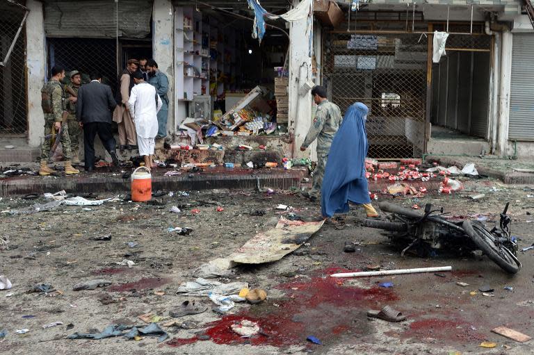 A burqa-clad Afghan pedestrian walks past security personnel at the site of a suicide attack outside a bank in Jalalabad on April 18, 2015