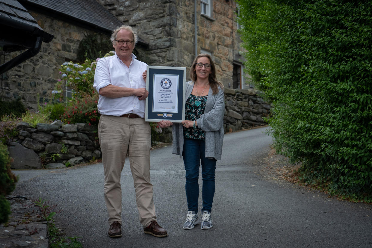 Gwyn Headley, left, and Sarah Badhan stand on Ffordd Pen Llech in the seaside town of Harlech, North Wales, with a certificate from Guinness World Records, confirming that the road is the steepest street in the world (Picture: SWNS)