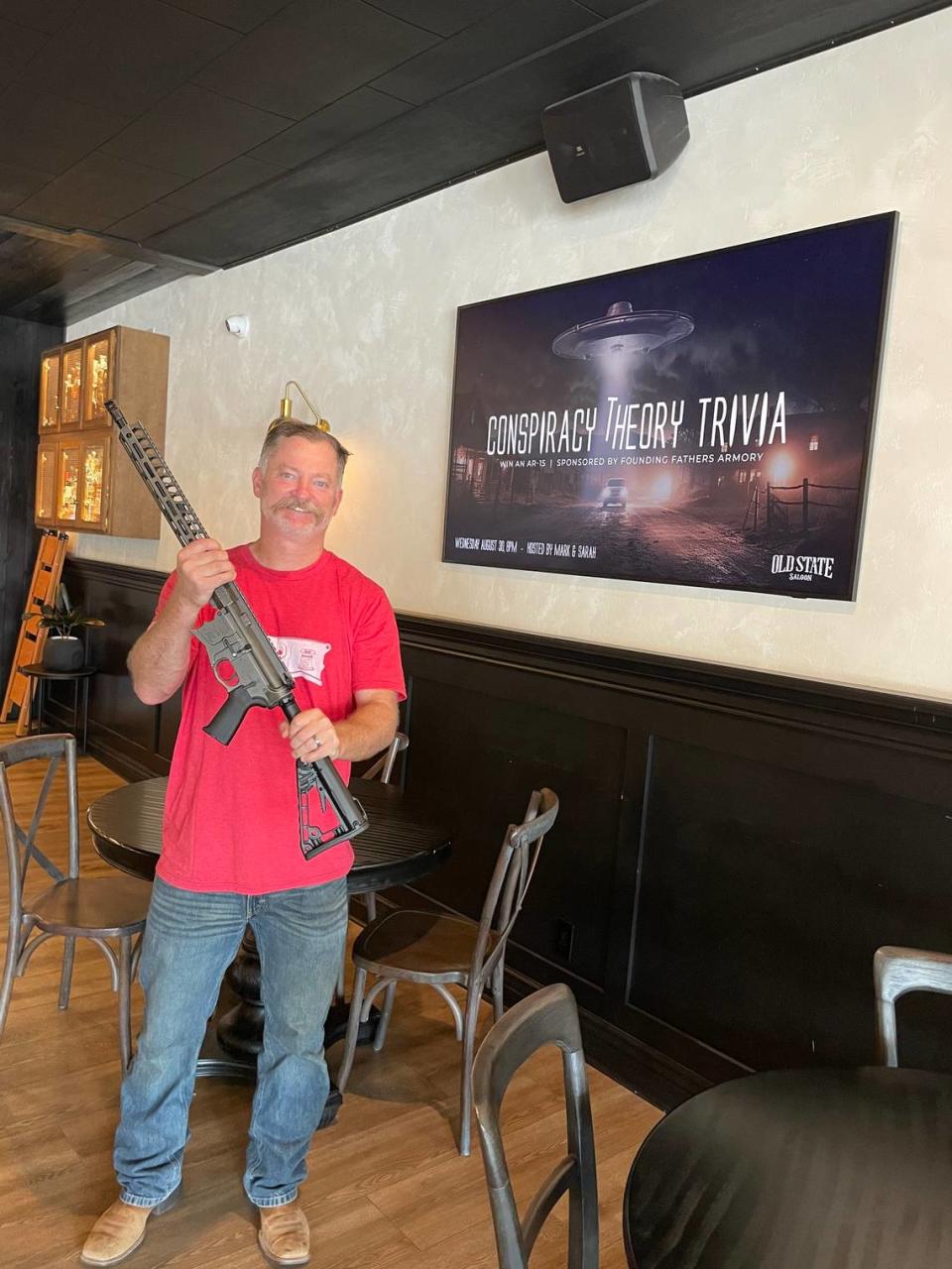 Old State Saloon owner Mark Fitzpatrick holds the AR-15 rifle that will be used as a prize.