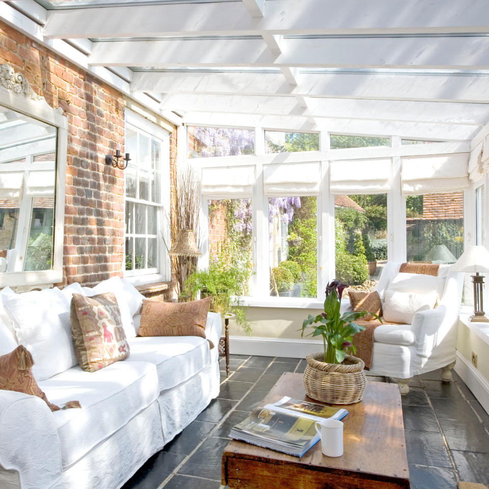 Lean-to conservatory with white sofa and armchair surrounding wooden trunk coffee table