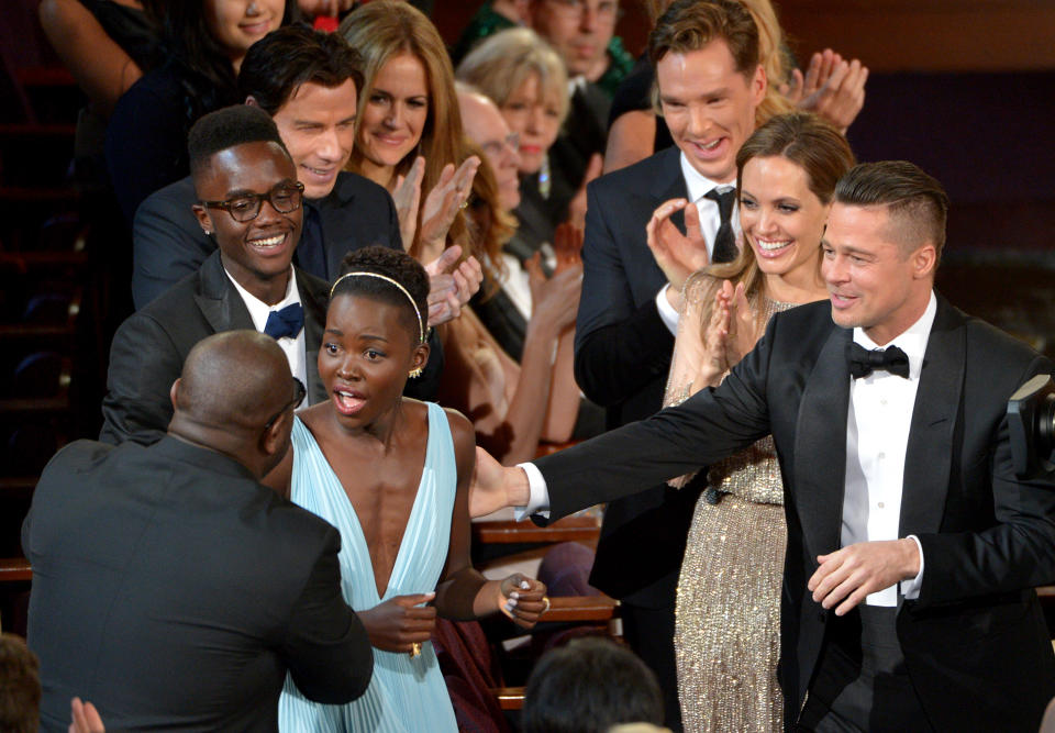 Director Steve McQueen, left, congratulates Lupita Nyong'o on her win for best actress in a supporting role for "12 Years a Slave" as, from background left, her brother Peter, John Travolta, Kelly Preston, Benedict Cumberbatch, Angelina Jolie, and Brad Pitt look on during the Oscars at the Dolby Theatre on Sunday, March 2, 2014, in Los Angeles. (Photo by John Shearer/Invision/AP)