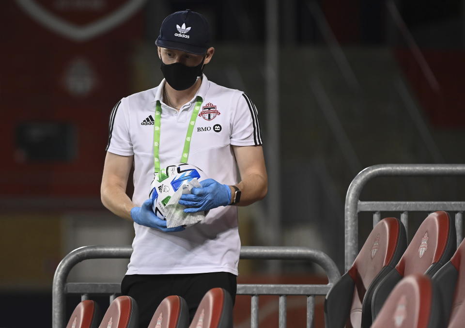 A person sanitizes the game soccer ball with a wipe after it went into the empty stands as Toronto FC takes on the Vancouver Whitecaps during second-half MLS Canadian Championship soccer match action in Toronto, Friday, Aug. 21, 2020. (Nathan Denette/The Canadian Press via AP)