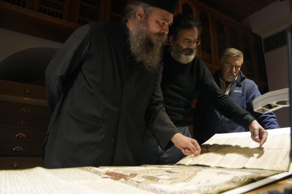 Father Theophilos, a Pantokrator monk, left, Byzantine scholar Yiannis Niehoff-Panagiotidis, center, and Anastassios Nikopoulos, a jurist and scientific collaborator of the Free University of Berlin, check a manuscript at the library of Pantokrator Monastery in the Mount Athos, northern Greece, on Thursday, Oct. 13, 2022. Deep inside a medieval fortified monastery in the Mount Athos monastic community, researchers are for the first time tapping a virtually unknown treasure: thousands of Ottoman-era manuscripts that include the oldest of their kind in the world. (AP Photo/Thanassis Stavrakis)