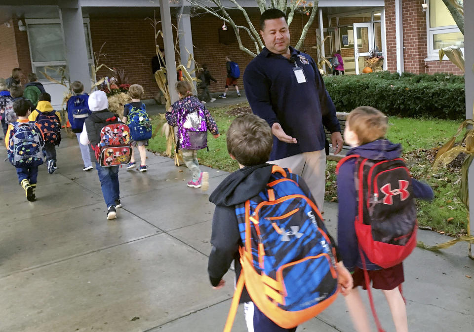 FILE - Campus monitor Hector Garcia greets students as they get off the bus at the start of the school day at West Elementary School in New Canaan, Conn., on Nov. 6, 2017. The shooting massacre at a Texas elementary school has spurred renewed calls for school safety, but experts debate whether more heavily fortified schools are the right solution. (AP Photo/Michael Melia, File)