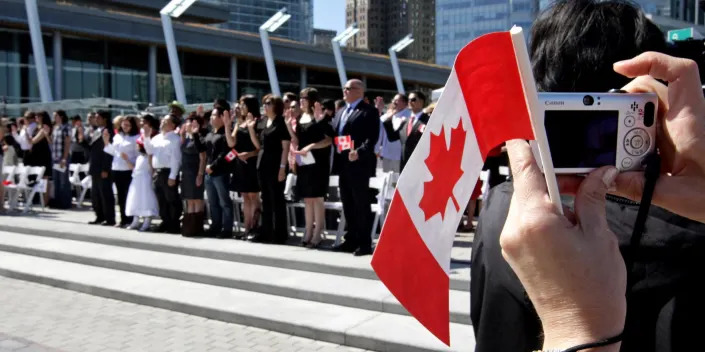 A woman takes a photograph while holding a Canadian flag