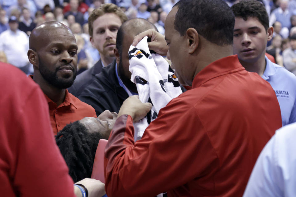 North Carolina State head coach Kevin Keatts, right, places a towel over injured player Terquavion Smith, bottom left, as Smith is wheeled off the court on a stretcher during the second half of an NCAA college basketball game against North Carolina, Saturday, Jan. 21, 2023, in Chapel Hill, N.C. Smith crashed to the floor after being fouled. (AP Photo/Chris Seward)
