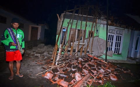 A villager stand near a damaged house - Credit: Antara Foto/Reuters