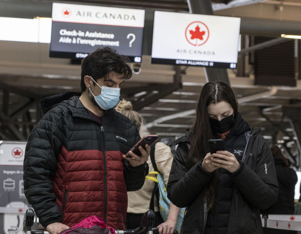 Travelers use their phones as they line up at the Ottawa International Airport, as airlines cancel or delay flights during a major storm in Ottawa, on Friday, Dec. 23, 2022. (Justin Tang /The Canadian Press via AP)