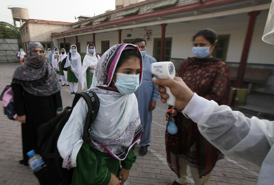 A worker checks body temperature of students upon her arrival at a school in Peshawar, Pakistan, Wednesday, Sept. 23, 2020. Pakistani officials welcomed millions of students back to middle schools following educational institutions reopened in the country amid a steady decline in coronavirus deaths and infections. (AP Photo/Muhammad Sajjad)