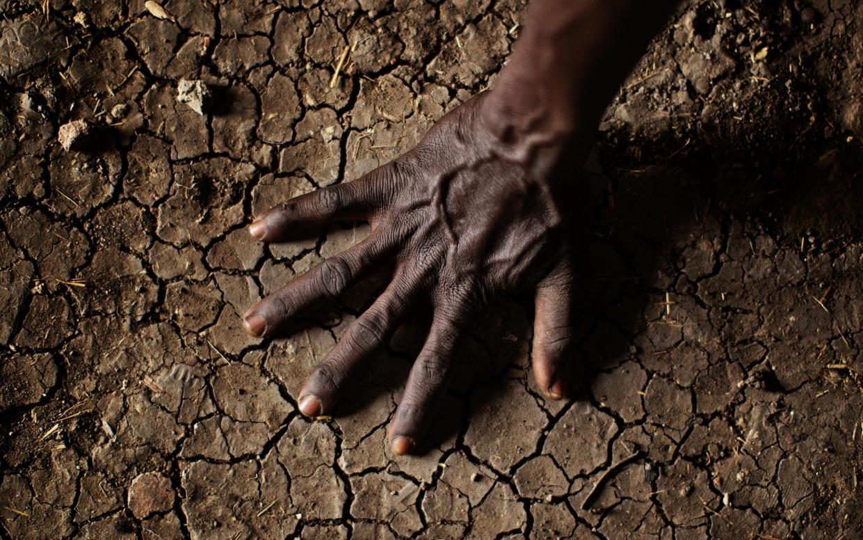 A man places his hand on the parched soil in the Greater Upper Nile region of north-eastern South Sudan, Africa