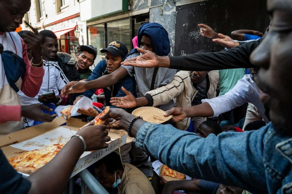 PHOTO: A police officer hands out pizza to dozens of recently arrived migrants to New York City as they camp outside of the Roosevelt Hotel, which has been made into a reception center, where they try to secure temporary housing on Aug. 01, 2023. (Spencer Platt/Getty Images)