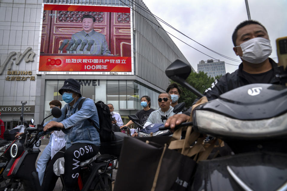 People wait to cross an intersection near a large video screen showing Chinese President Xi Jinping speaking during an event to commemorate the 100th anniversary of China's Communist Party at Tiananmen Square in Beijing, Thursday, July 1, 2021. (AP Photo/Mark Schiefelbein)