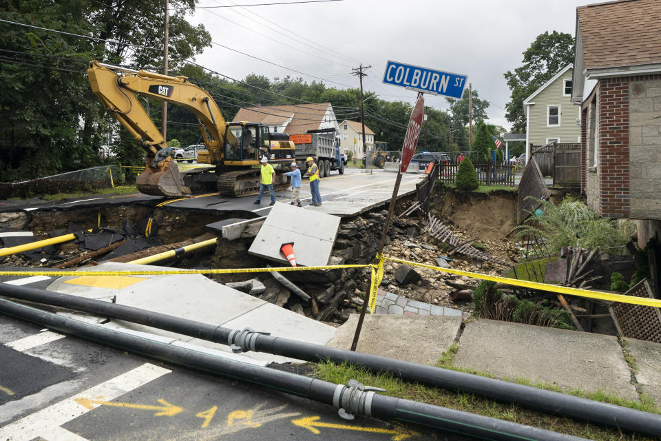 Public works officials examine the damage to a road and front yard that was washed away by recent flooding, Wednesday, Sept. 13, 2023, in Leominster, Mass. (AP Photo/Robert F. Bukaty)