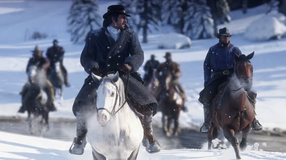 A screenshot from "Red Dead Redemption 2" showing a number of cowboys on horseback riding across a snowy landscape.