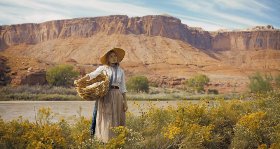 a person holding a basket in a field of flowers with a river in the background